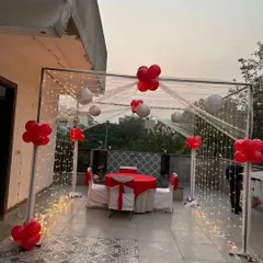 A romantic dinner for two on a terrace. This setup features a cabana frame draped with sheer fabric and fairy lights, with red and white decorations for an intimate and private dining experience.
