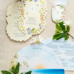 A collection of day-of stationery for a destination wedding, including a fan-shaped program, floral itinerary cards, and welcome bag tags. All pieces are designed with a cohesive visual theme.