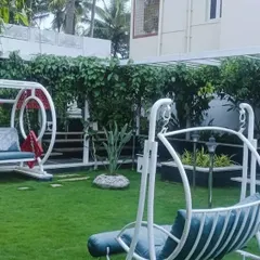 A beautiful residential garden designed for relaxation, featuring two modern swings on a pristine lawn. The space is framed by a lush green wall of climbing plants, providing privacy and a sense of enclosure.