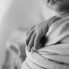 A close-up of a newborn's tiny, wrinkled hand in black and white. This macro shot preserves one of the most unforgettable details of the newborn phase.