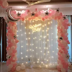 A dreamy 'Welcome Baby' setup perfect for bringing your little girl home. We created this magical moon and stars theme using a pink and white balloon arch, a large silver crescent moon foil balloon, and a backdrop of twinkling fairy lights for a truly special celebration.