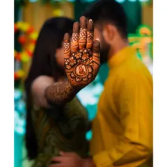A romantic and creative mehendi photo, with the bride's henna-covered hand in the foreground and the couple sharing a quiet moment in the background.