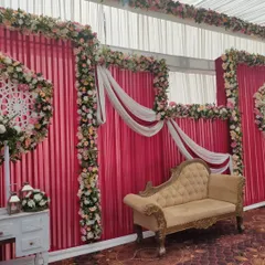 This reception stage combines a pink fabric backdrop with delicate floral borders and draped white cloth. The vintage style chaise lounge adds a touch of classic elegance for the couple's seating.