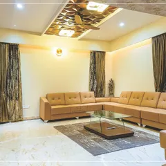 This comfortable living room is designed for relaxation, with a large L-shaped sofa. A geometric wooden panel on the false ceiling adds a subtle but impactful design detail.