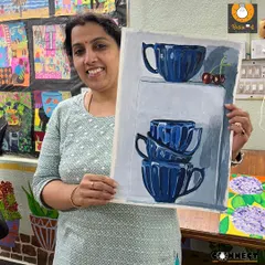 A happy student shows off her completed monochrome still life painting of stacked blue cups. This exercise is fantastic for understanding light, shadow, and form.