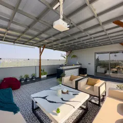 A view from inside a covered pergola, looking out over the terrace. This shot highlights the patterned tile floor, modern furniture, and the outdoor projector setup.