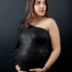 A beautiful close-up of the mom-to-be, looking away with a gentle expression. The studio lighting highlights the sparkle of her dress and her natural pregnancy glow.
