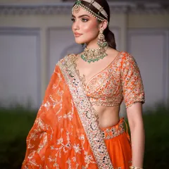 A portrait showcasing the beautiful contrast between the orange lehenga and the green emerald jewellery, a classic combination for Indian festivities.