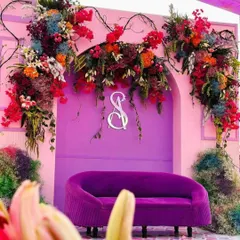 A bold and artistic photo spot with a purple velvet sofa set against a magenta archway adorned with a riot of colorful flowers.