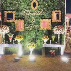 A personalized selfie wall for a night event, featuring a lush green backdrop, ornate golden frames, and a custom neon sign with the couple's names.