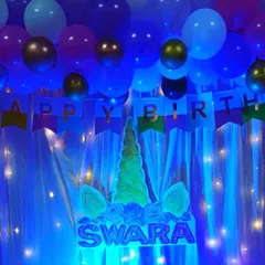 A magical unicorn theme for Swara's birthday. The centerpiece is a custom-made unicorn head with her name in glitter, set against a backdrop of blue balloons and twinkling fairy lights.