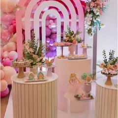 An elegant dessert station featuring a modern rainbow arch backdrop in shades of pink. The tiered display stands and fresh flowers create a sophisticated and stylish look.