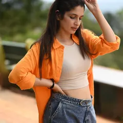A casual and cool outdoor portrait. The bright orange shirt pops against the soft, green background, and the natural light gives the shot a relaxed, easygoing vibe.