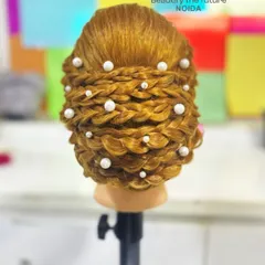 An intricate braided updo on a mannequin, adorned with pearls. We ensure students get ample practice on dummies to perfect their technique before working on live models.