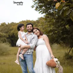 A heartwarming family portrait in a lush green field. The parents and their little girl are all dressed in white, perfectly capturing the joy of their family growing from three to four.