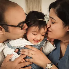 A priceless moment of pure joy and love. A mother and father kiss their smiling baby's head, a memory captured to be treasured forever.