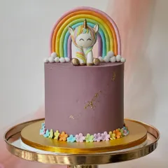 A modern unicorn cake with a rich purple buttercream. The design is completed with a fondant rainbow, a cute unicorn figure, and a border of tiny flowers.