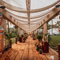 The long entrance walkway, lined with hand-carved Tiki statues and lush tropical plants. The ceiling is draped with fabric and strung with lights, creating a magical pathway for guests.