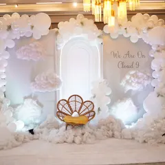 Welcome to Cloud 9. This all-white baby shower theme creates an ethereal and serene atmosphere with fluffy clouds on the floor, a balloon arch, and a neon-lit archway.