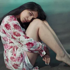 A relaxed, full-body shot from a beach lifestyle session. The pose is natural and contemplative, and the soft lighting enhances the calm, serene mood of the setting.