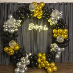 A chic and stylish 'Bride to be' ring backdrop for a bridal shower or bachelorette party. The circular frame is decorated with black, gold, and silver balloons and a central neon sign.