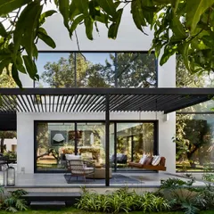 We design spaces that extend living into the outdoors. This covered terrace, featuring a slatted pergola that creates a beautiful play of light and shadow, provides a seamless transition from the living room to the garden, perfect for relaxation and entertaining.