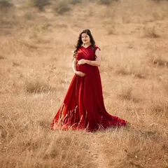 A stunning solo portrait featuring one of my flowing maternity gowns. The vibrant red stands out beautifully against the rustic, sunlit field, creating a dramatic and elegant look.