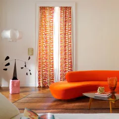 We love embracing bold expressions of color and form. This living space channels a vibrant, pop-inspired energy with a serpentine orange sofa and graphic drapery from Élitis, proving that luxury can be both sophisticated and playful.