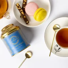 This top-down flat lay of Earl Grey tea is styled for a modern, elegant brand. The clean white space, paired with colourful macarons and gold spoons, creates a sophisticated image ideal for social media or a brand lookbook.