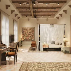 A serene bedroom suite within the haveli, featuring a classic four-poster bed and a mix of traditional textiles. The space is designed to be a peaceful retreat, with large windows, a high-beamed ceiling, and curated art that reflects Indian heritage.