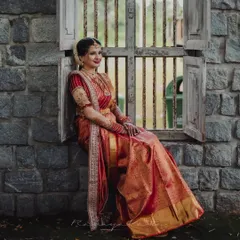 A moment of quiet elegance. This bride is the picture of grace in a traditional red and gold Kanjeevaram silk saree, paired with a bespoke embroidered blouse. The rich texture of the silk and the detailed craftsmanship of the blouse create a timeless bridal look.