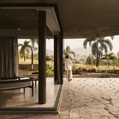 The Pavilion House in Nashik is designed as a low-lying structure that merges with the landscape. This view shows how the living space opens onto a stone patio, creating a seamless flow between the interior and the serene backwaters of Lake Beze.