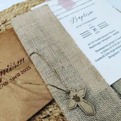 A bespoke Baptism invitation featuring rustic kraft paper, a jute sleeve, and a wooden cross charm for a natural and faith-filled design.