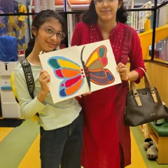 A mother and daughter proudly display the colorful butterfly painting they created together during one of our guided art sessions.