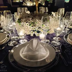 A close-up of a formal dinner setting we executed. The deep purple tablecloth, silver charger plates, and crisp white floral arrangements create a look of royal splendor and timeless elegance.