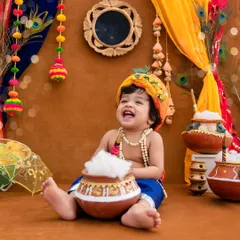 A joyful laugh from this baby Krishna, surrounded by colorful decorations and pots of 'makhan' for a festive Dahi Handi celebration.