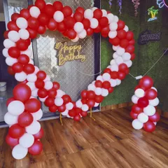 A heart-shaped balloon arch is a classic choice for a romantic photo backdrop. This indoor setup uses red and white balloons and a 'Happy Birthday' sign, creating a perfect frame for pictures.