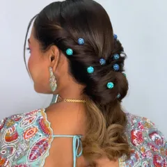 A still image showcasing a versatile and trending bridal hairstyle from the side. This modern updo, decorated with blue beaded pins, is suitable for everything from a Haldi ceremony to a cocktail party.