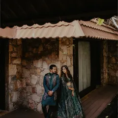 A couple shares a look while standing on the wooden porch of a rustic stone cottage. This portrait blends elegant attire with a natural, architectural setting for a unique look.