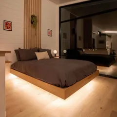This bedroom features a floating bed frame with under-lighting, creating a modern and spacious feel. The large glass window provides an uninterrupted view of the outdoors, blending the room with its natural surroundings.