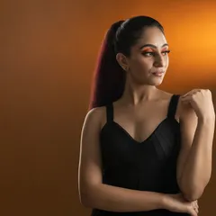 A chic and modern fashion portrait of a model in a black top against a warm studio backdrop, showcasing dramatic makeup and a high-ponytail hairstyle.