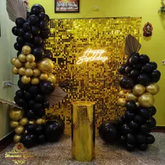 This is a glamorous birthday party setup featuring a gold shimmer wall, a "Happy Birthday" neon sign, and dramatic black and gold balloon pillars. I can create these elaborate backdrops for any special occasion.