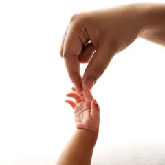 A parent's hand gently holding their baby's tiny, delicate fingers. It shows the scale of just how small and new they are.