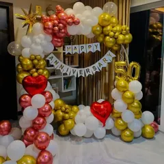 A festive 50th anniversary celebration setup indoors. I created a full balloon arch using a classic combination of red, gold, and white balloons, complemented by a 'Happy Anniversary' banner and large '50' foil numbers.