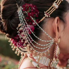 The beauty of a bridal bun is in the details. This intricate hairstyle features fresh carnations and a multi-layered hair accessory that perfectly complements the bride's heavy jewelry.