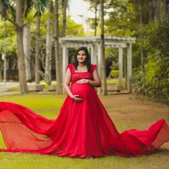 A stunning solo portrait of a mother-to-be in a vibrant red flowing gown, standing in a lush green park. This shot is all about celebrating the power and beauty of pregnancy.