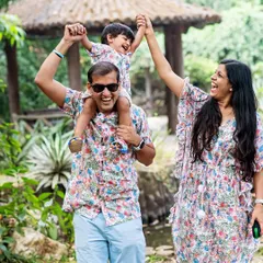 A playful family photo capturing pure joy as the parents lift their son up while walking through a park.