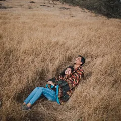 A cozy, intimate moment of the couple lying together in a field of tall, dry grass. This high-angle shot feels natural and captures a quiet moment of shared happiness.