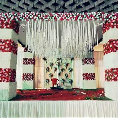 A grand and opulent mandap design featuring massive pillars covered in red and white flowers. The hanging floral strings and intricate backdrop create a rich, traditional look.