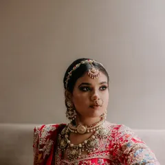 A classic, elegant portrait of the bride, Sakshi, looking away thoughtfully, her intricate jewelry and red lehenga beautifully captured.